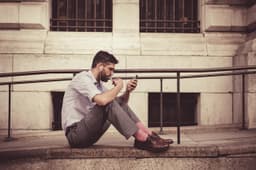 Man sitting on steps using his smartphone, illustrating Moov Money person-to-person payments to a debit card