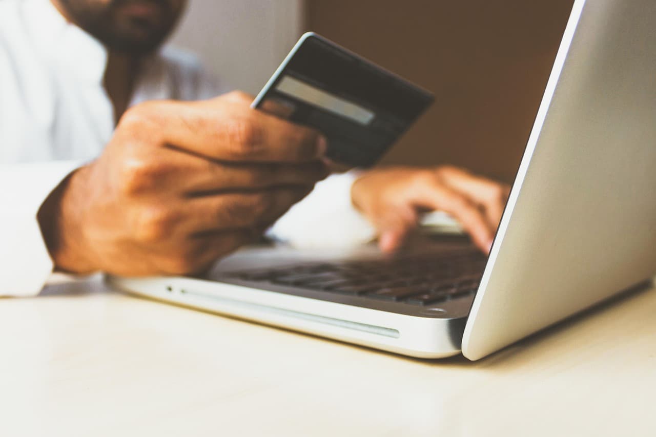A hand holding a payment card next to an open laptop