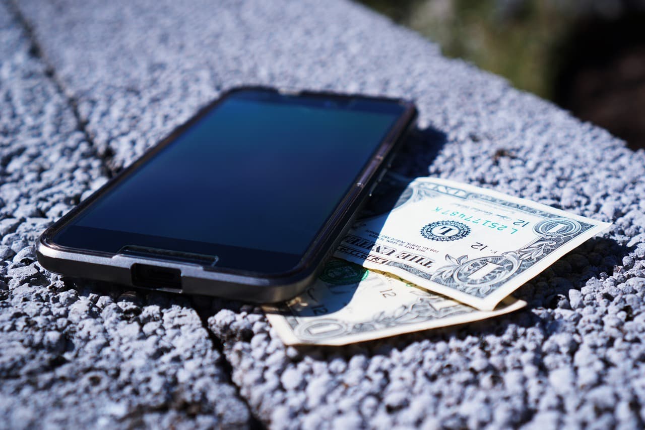 A smartphone lying next to a folded US dollar bill