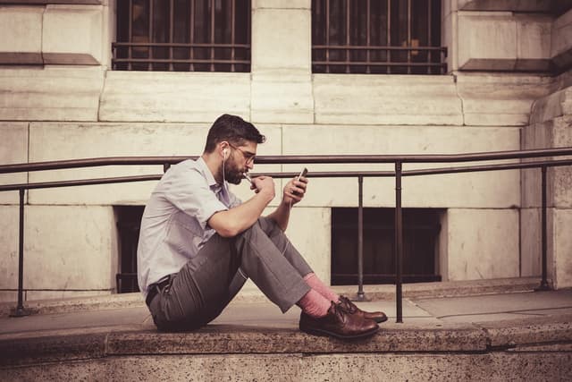 Man sitting on steps using his smartphone, illustrating Moov Money person-to-person payments to a debit card