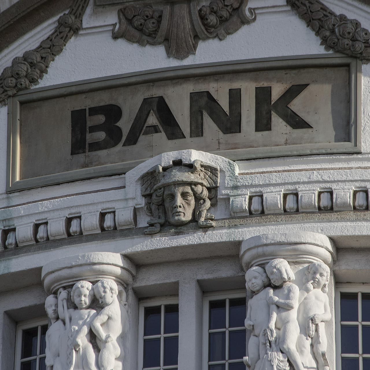 The word BANK carved above the entrance of a classical stone bank building